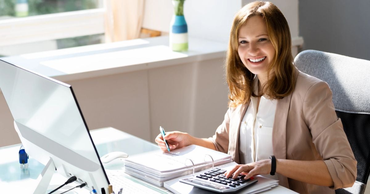 An image of a woman sitting at her desk, focused on her computer screen while working on accounting tasks.